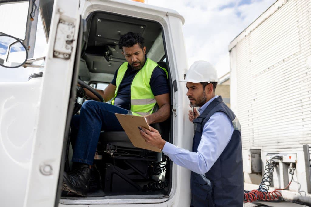 Truck driver reviewing paperwork with a logistics coordinator