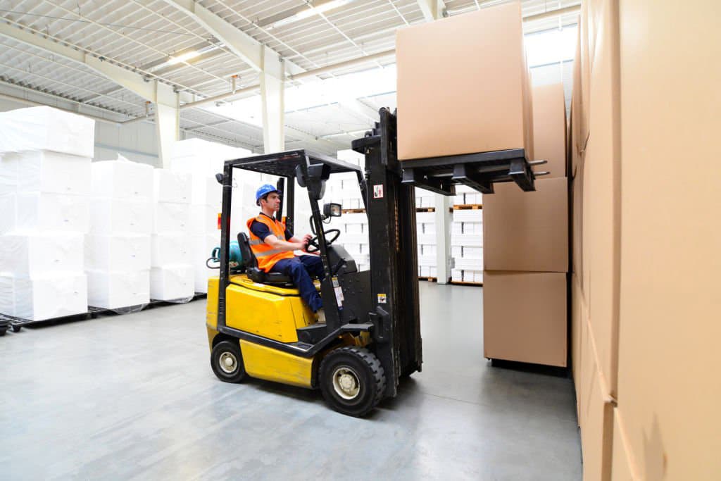 Forklift operator moving boxed inventory in a warehouse